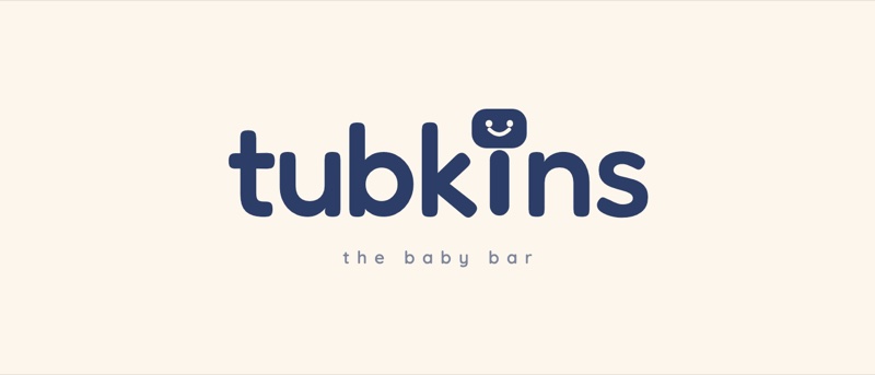 The Tubkins wordmark in navy on cream, with a smiling soap bar forming the dot of the letter i.